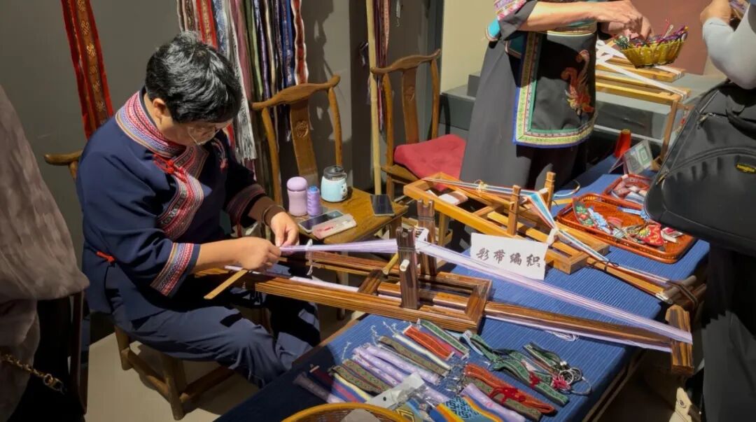 图为省级传承人雷岳梅向队员展示彩带编织技巧